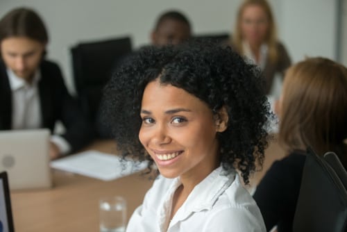 A smiling female instructional designer seated at a table in a workplace.